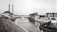 Auf dem Bild aus dem Jahr 1913 ist hinter dem Wasserkraftwerk die Dampfzentrale mit den beiden hohen Schornsteinen zu sehen. Bild: ...