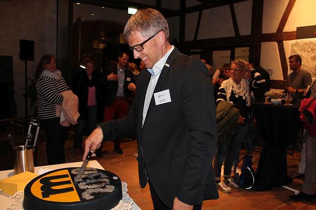 Bürgermeister Robert Scherer schneidet eine Torte mit dem Logo "Meersburg 2030" an, die er dann als süße Überraschung an die Bürger ...