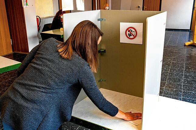 Eine Wahlhelferin desinfiziert die Wahlkabine.