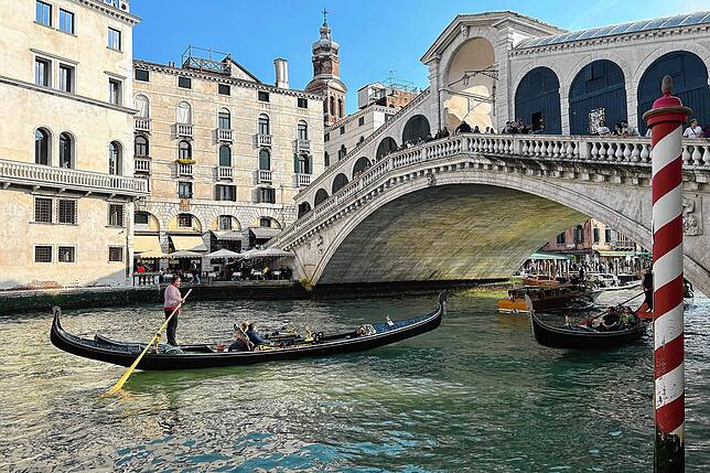 Eine Gondel mit Touristen vor der Rialto-Brücke im Zentrum von Venedig. Wer hier tagsüber unterwegs ist, muss an manchen Tagen extra zahlen.