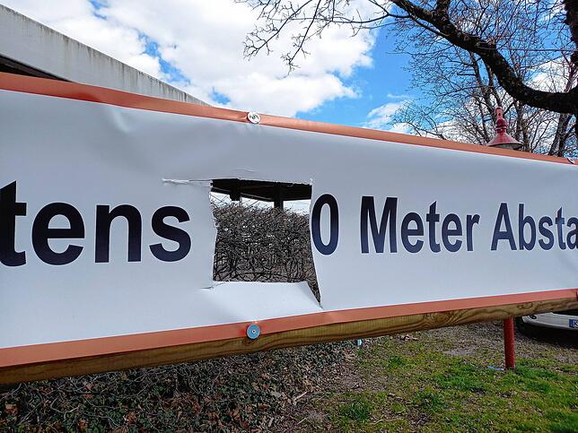 Vor dem Bahngleis auf der Mole in Radolfzell: Ein Abstandsbanner mit Durchblick. Die Hecke dahinter ist auch noch nicht grün.
