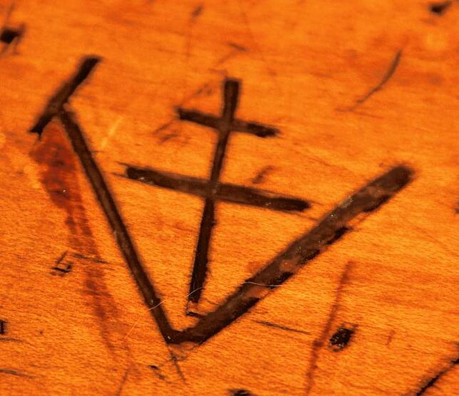 Hier ist das Symbol eines Balkenkreuzes zu sehen. Auch ein Merkmal für das Alter des Tisches.