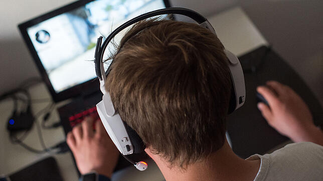 Ein junger Mann sitzt mit einem Headset vor einem Laptop und spielt ein Online-Computerspiel. Bis in die Nacht sitzen Jungs am Computer ...