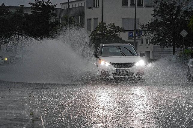 Nicht ungefährlich: Ein Auto fährt bei starkem Regen auf einer überfluteten Straße.