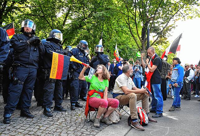 Eine Demonstrantin bläst in eine Vuvuzela vor einer Polizeikette.