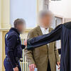 Der angeklate Senior Walter-Eckard M. wird von seinem Verteidiger und einem Justizbeamten zur Anklagebank geleitet.