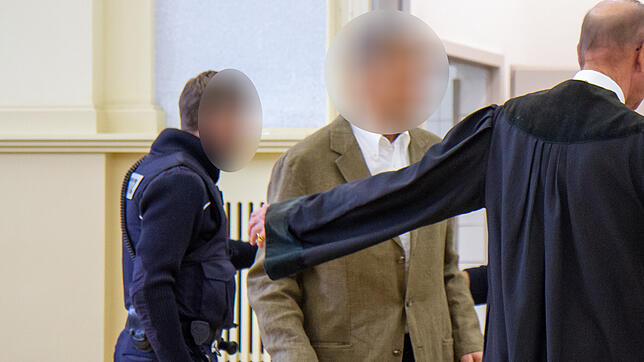 Der angeklate Senior Walter-Eckard M. wird von seinem Verteidiger und einem Justizbeamten zur Anklagebank geleitet.