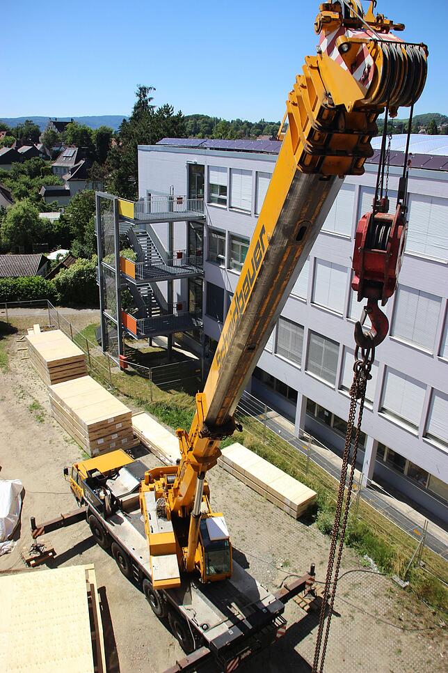 In unmittelbarer Nachbarschaft zum Gymnasium steht ein Autokran, mit dem die Zimmermänner vorbereitende Arbeiten erledigen.