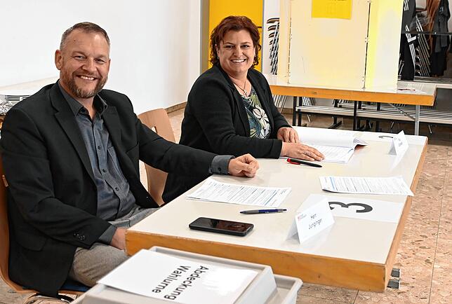 Michael Junginger und Manuela Gottwald sind Wahlhelfer im Wahllokal in der Heidenfelshalle in Zizenhausen. Vorne ist die Wahlurne zu sehen.
