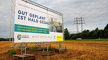Ein Plakat weist auf den hier geplanten Gesundheitspark und das zukünftige Zentralkrankenhaus hin. Im Hintergrund ist die B 34 zu sehen.