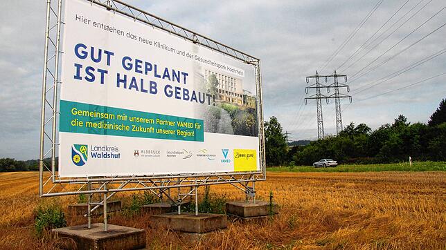 Ein Plakat weist auf den hier geplanten Gesundheitspark und das zukünftige Zentralkrankenhaus hin. Im Hintergrund ist die B 34 zu sehen.