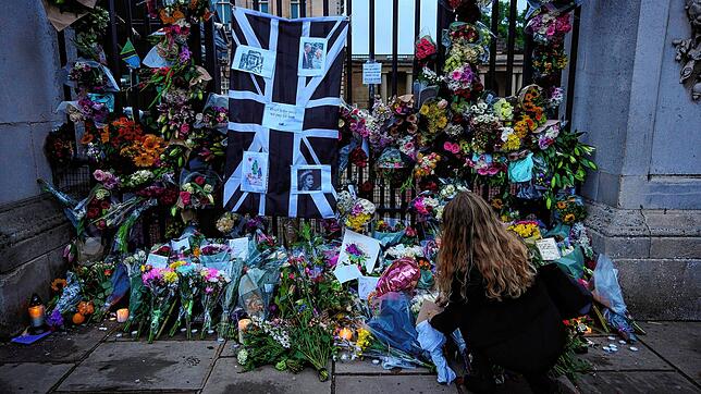 Eine Frau legt Blumen nieder und hinterlässt einen Grußbotschaft vor den Toren des Buckingham Palace.