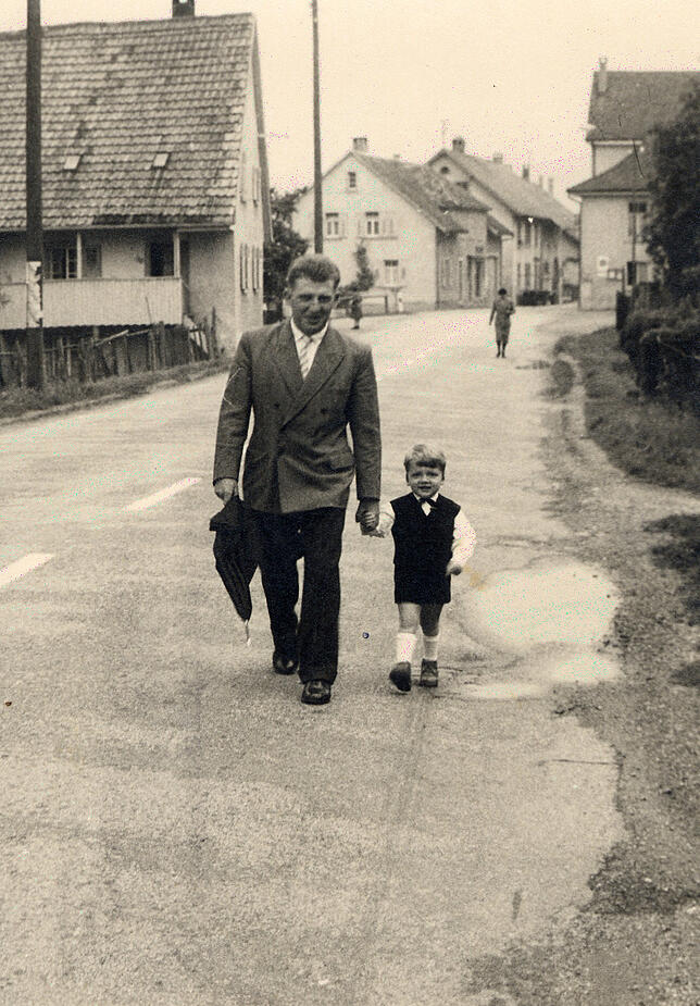 Erich Thomann (links) und Sohn Thomas circa 1962 auf dem Weg durch das Dorf zum Kirchgang. Rechts im Hintergrund das Gasthaus "Traube". ...