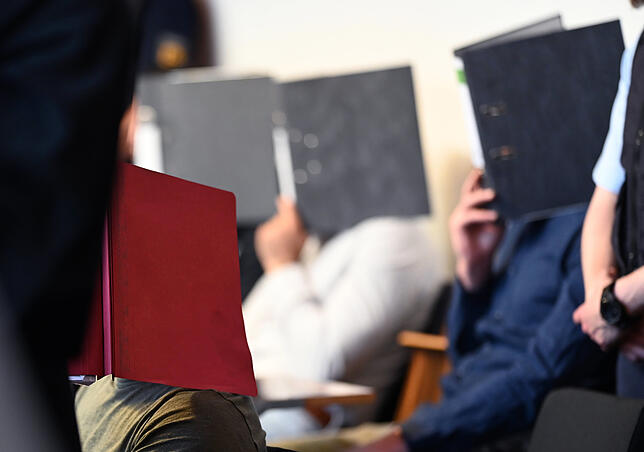 Einige der Angeklagten bedecken ihre Gesichter mit Aktenordnern. Sie sollen im Oktober 2018 eine 18-Jährige neben einer Disco im ...