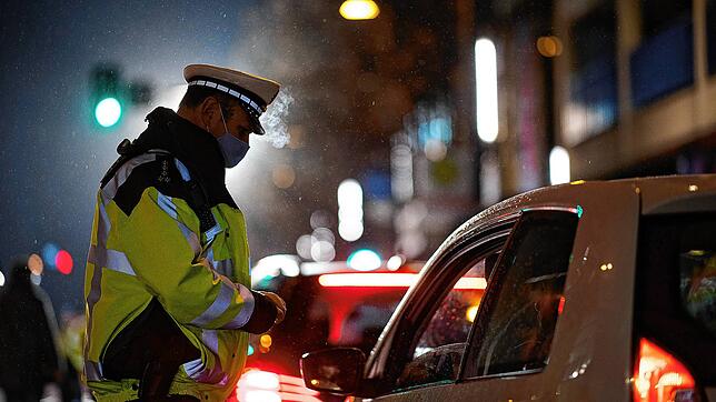 Ein Polizist kontrolliert im Dezember in Stuttgart, ob der Fahrer einen triftigen Grund für seine nächtliche Fahrt hat. Bilder: dpa