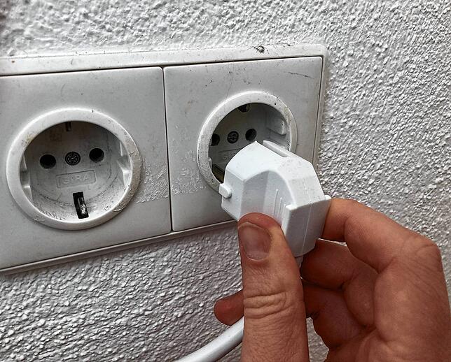 Ein Mann steckt einen Stecker in eine Steckdose: Im Falle eines Stromausfalls kommt aus der Buchse kein Strom mehr heraus.