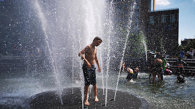Menschen kühlen sich an einem Brunnen. Mit Temperaturen von über 38 Grad meldet sich der Hochsommer in Deutschland zurück.