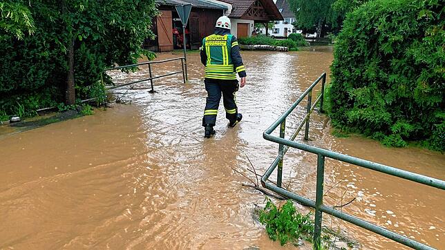 Ein Feuerwehrmann läuft am Montag durch das Wasser des übergelaufenen Dorfbaches.