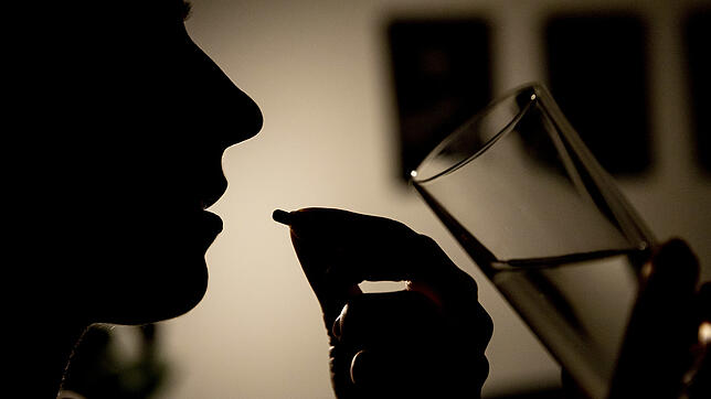 Gestellte Szene: Eine Frau spült eine Tablette mit einem Glas Wasser hinunter.