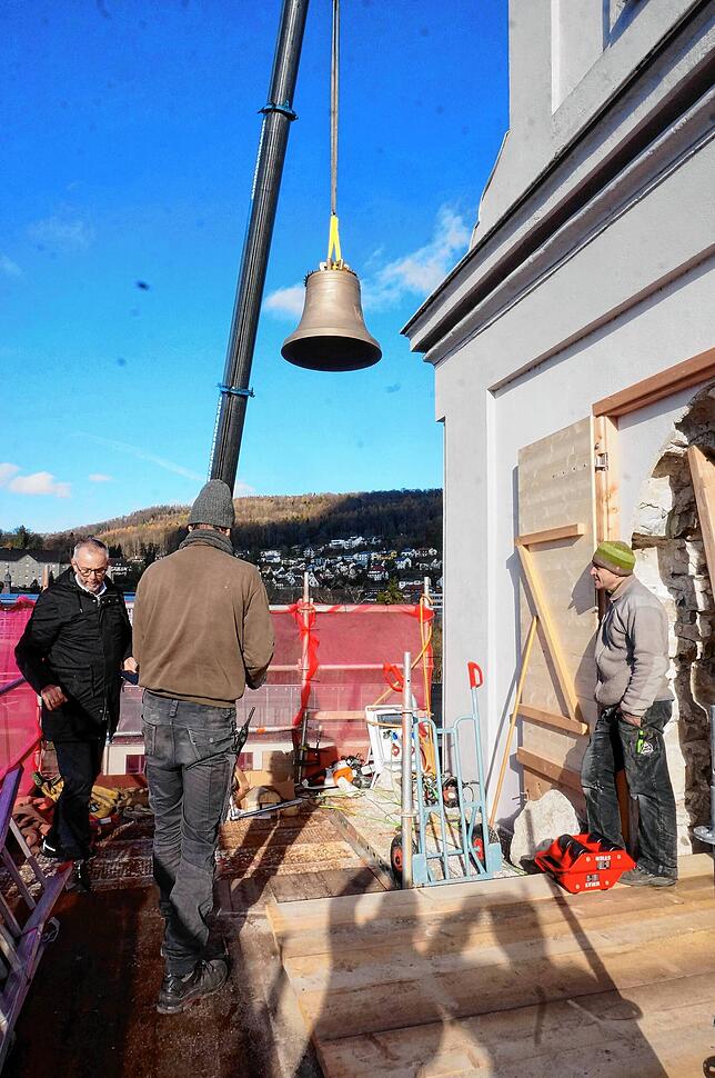 Langsam schwebt die Glocke Richtung Gerüstboden, die roten Lastenroller stehen bereit, die Handwerker warten geduldig, links Pfarrer ...