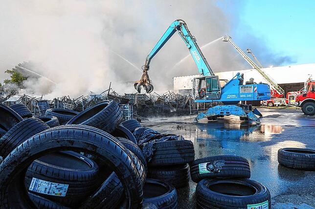 Einsatzkräfte der Feuerwehr stehen während eines Großbrandes auf dem Gelände eines Reifengroßhändlers und löschen das Feuer.
