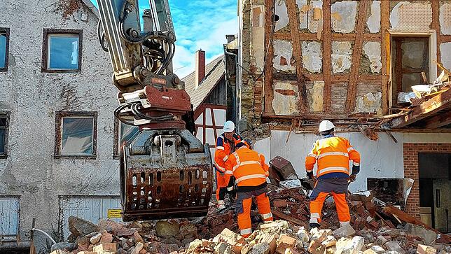 Die Bauarbeiter suchen leichtere Holzteile aus den Trümmern, um sie in einen Müllcontainer zu werfen. Selbst, wenn es auf der Baustelle ...