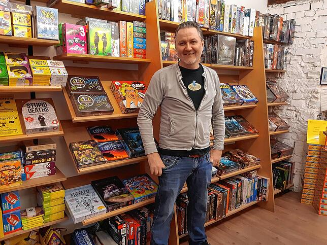 Inhaber Michael Palm in seinem Fachgeschäft für Spiele und Comics vor einem gefüllten Regal.
