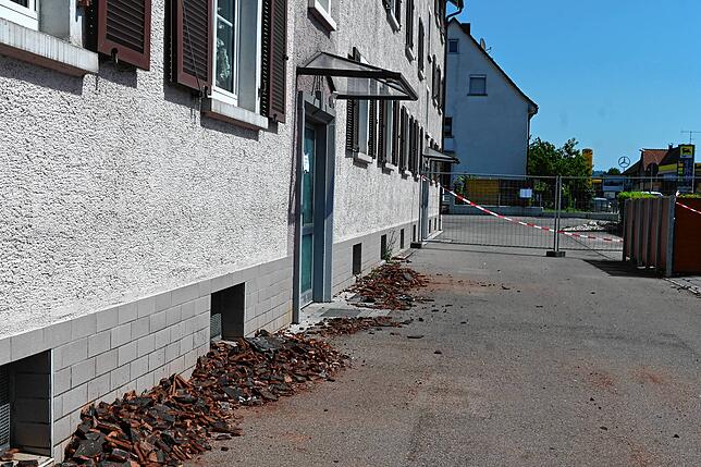 Ein Foto durch den Bauzaun: Am Haus liegen die zusammengefegten Ziegel vom Dach.