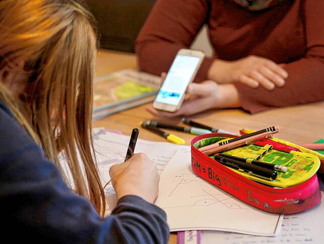 Eine alleinerziehende Mutter hilft ihrer zwölfjährigen Tochter beim Homeschooling und hält ein Smartphone in der Hand.