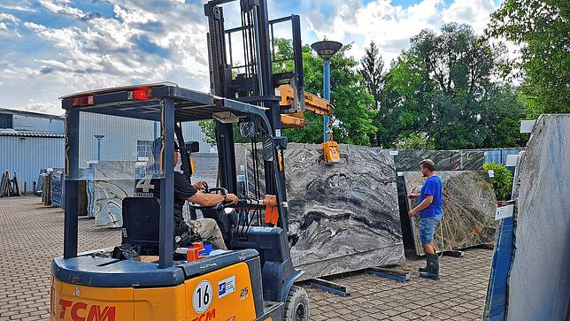 Zwei Mitarbeiter der Firma bringen eine Steinplatte zur Weiterverarbeitung aus dem Steinpark in die Fertigungshallen.