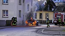 Ein Auto brennt in der Hasemannstraße, direkt neben einem Wohnhaus. Die Feuerwehrleute löschen von der Gebäudeseite her.