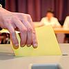 Ein Wahlzettel wird in eine Wahlurne gesteckt.