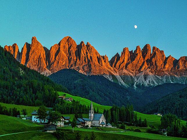 Die Heimat der Messners: Sonnenuntergang bei der Geislergruppe in den Dolomiten. Im Vordergrund das kleine Dorf St. Magdalena. Das ...