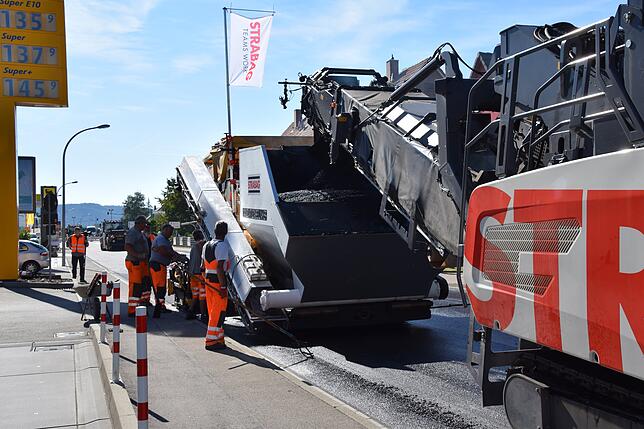 Das vordere Fahrzeug ist der Beschicker, der den heißen Asphalt an das Fertigerfahrzeug gibt. Der Beschicker wiederum erhält es von ...