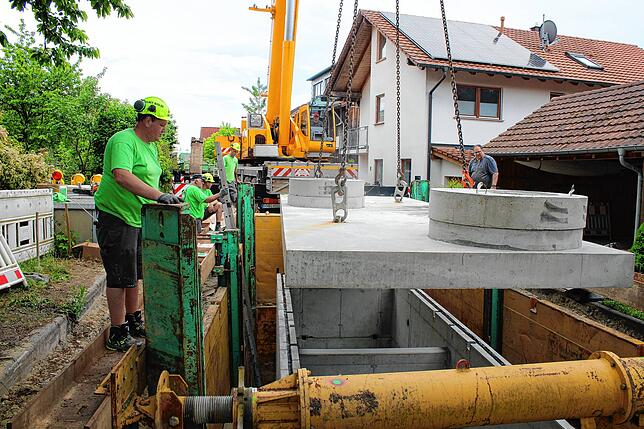 Straßenbaumeister Adrian Delhey (links) beobachtet, wie die Decke des Löschwasserbehälters sich langsam auf den Rahmen senkt.