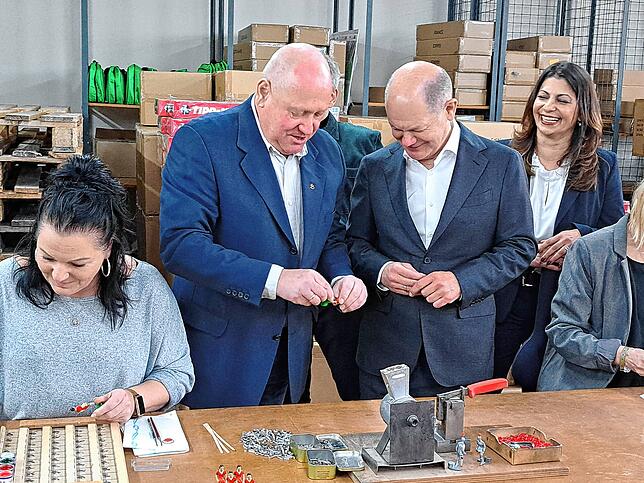 Mathias Mieg zeigt dem Bundeskanzler, wie der Druckknopf auf den Tipp-Kick-Figuren montiert wird. Links bemalt Mitarbeiterin Bianca ...