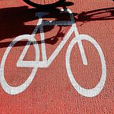 Ein Radfahrer wirft einen Schatten auf das Fahrradzeichen auf roten Teer (Symbolbild).