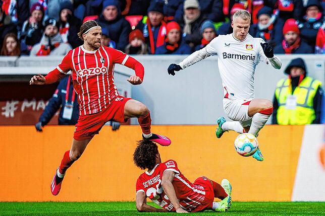 Leverkusens Mitchel Bakker (r) in Aktion gegen Freiburgs Lucas Höler (l) und Freiburgs Kiliann Sildillia (M).