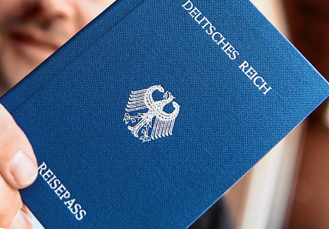 Ein Mann hält ein Heft mit dem Aufdruck „Deutsches Reich Reisepass“ in der Hand.