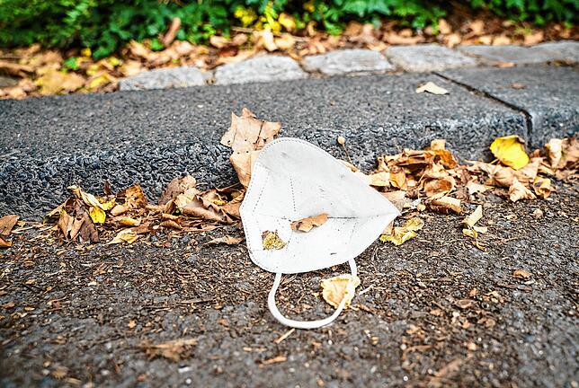 Symbolfoto: Eine FFP-2-Maske liegt im September in Würzburg am Straßenrand inmitten von vertrockneten Blättern.
