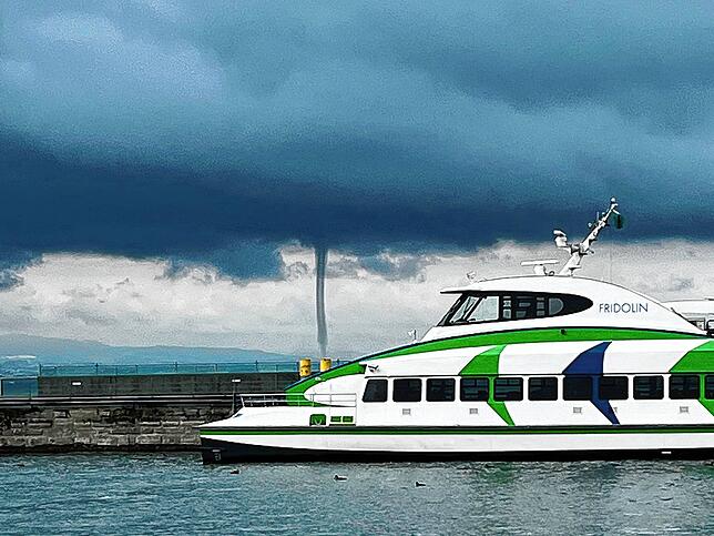 Ein Katamaran liegt im Hafen von Friedrichshafen, während im Hintergrund die Wasserhose über den Bodensee zieht.