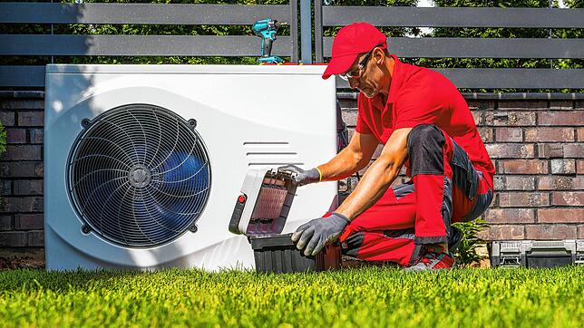 Ein Monteur installiert eine Wärmepumpe in einem Garten. Aber für welche Art von Häusern taugt das System eigentlich?
