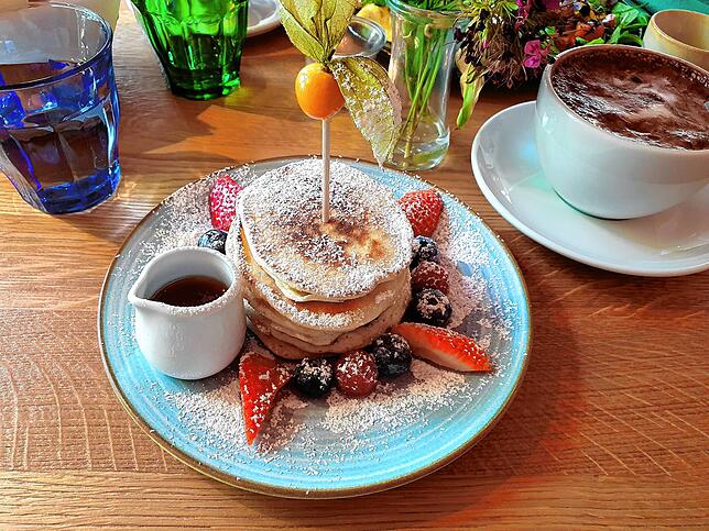Die Pancakes werden mit frischen Beeren und Ahornsirup serviert.