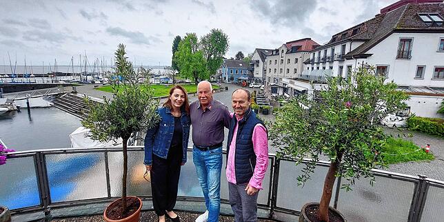 Snezana und Zoran Rajkovaca sowie Andreas Jehle stehen auf der Terrasse – im Hintergrund der Willam-Graf-Platz mit weiteren Gastronomien ...