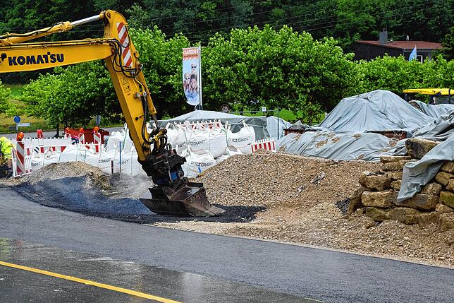 Mit Asphalt befestigt ein Bagger einen Bypass-Graben, der eine Unterspülung der gerade erst reparierten Ersatzfahrbahn neben der ...