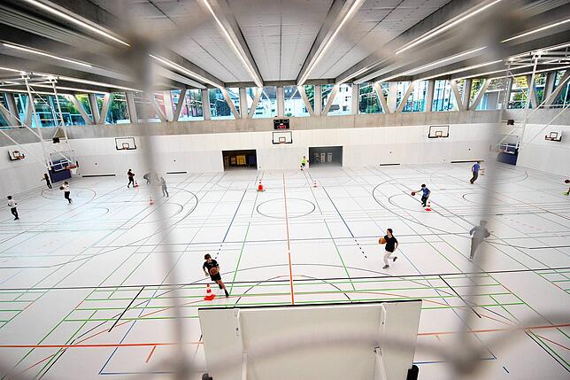 Der Blick von der Tribüne geht durch ein Ballfangnetz auf die neue Dreifeldsporthalle.