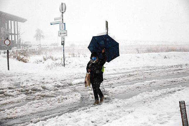 Mit Mund- und Nasenschutz sowie Regenschirm stapft eine Frau am &bdquo;Haus der Natur&ldquo; am Feldberg durch den Schnee. ...