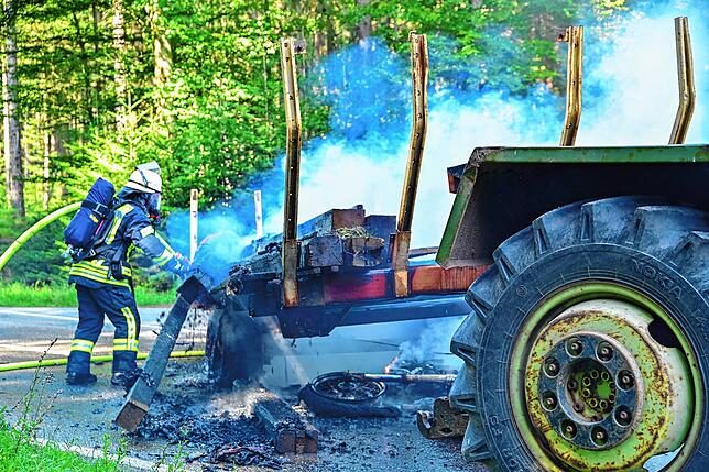 Die Feuerwehr löscht den mit Holzbalken beladenen Anhänger, der durch den Zusammenprall mit einem Motorrad in Brand geraten ist.