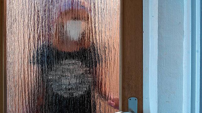 Eine Frau steht mit Maske hinter einer Glastür. Baden-Württemberg hat die Isolationspflicht für Corona-Infizierte abgeschafft