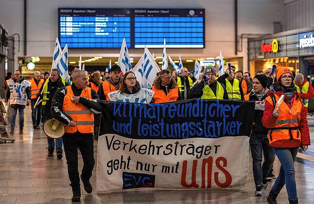 Streikende der Gewerkschaft EVG ziehen mit Fahnen und Plakaten durch den Hauptbahnhof in Duisburg.